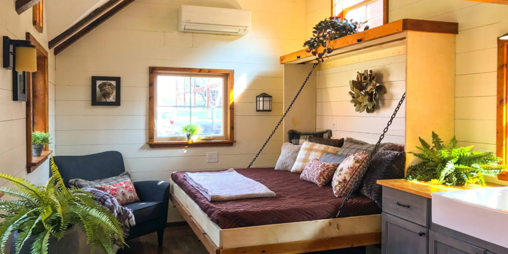tiny home bedroom with window and bed folded down from the wall with pillows and a throw blanket on it nicely made.